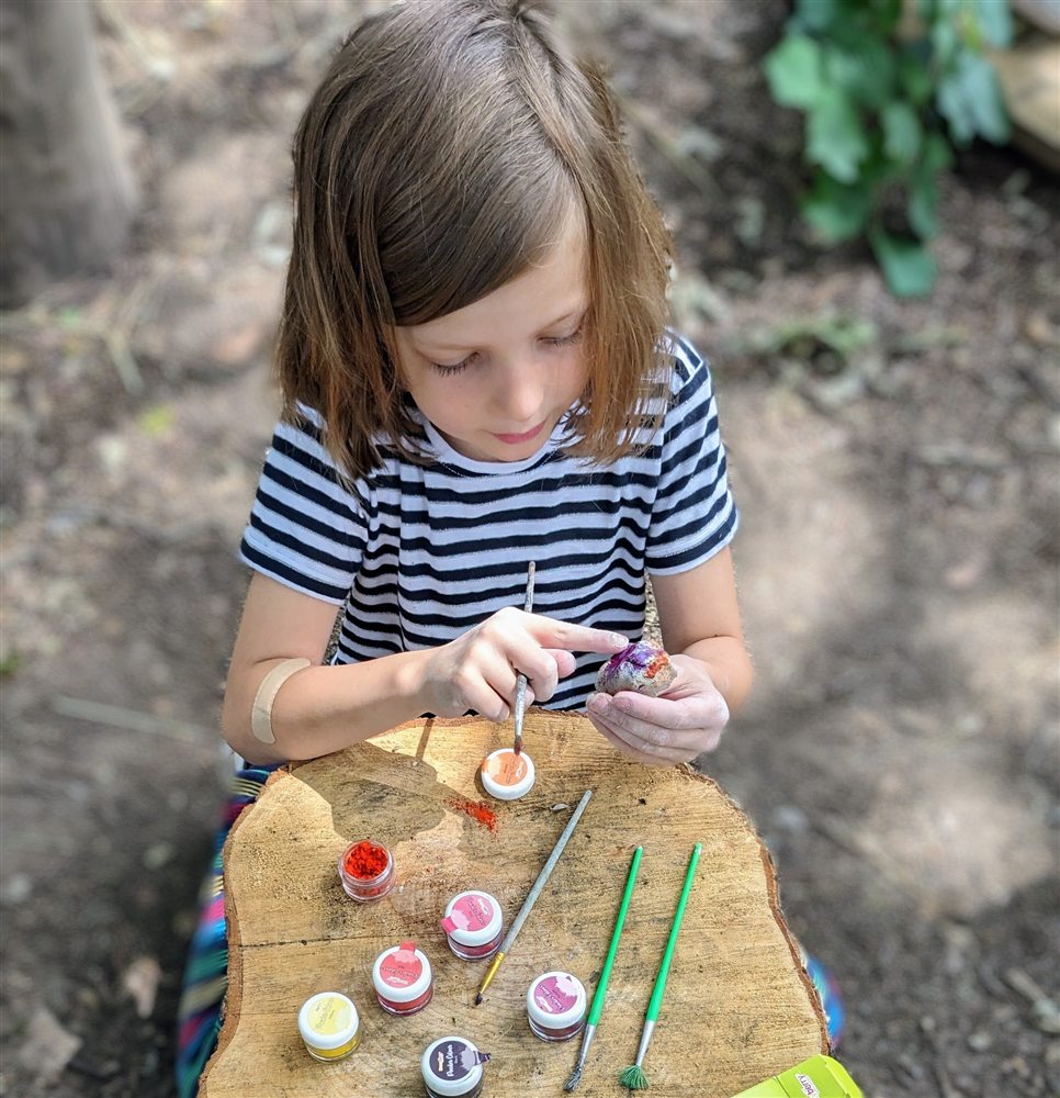 A child painting with natural pigments at a wooden stump in the woodland