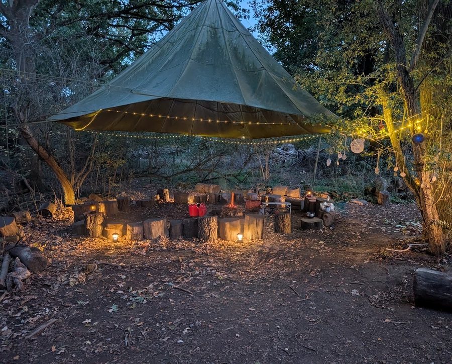 The log circle under the shelter at dusk, lit by lanterns and fairy lights