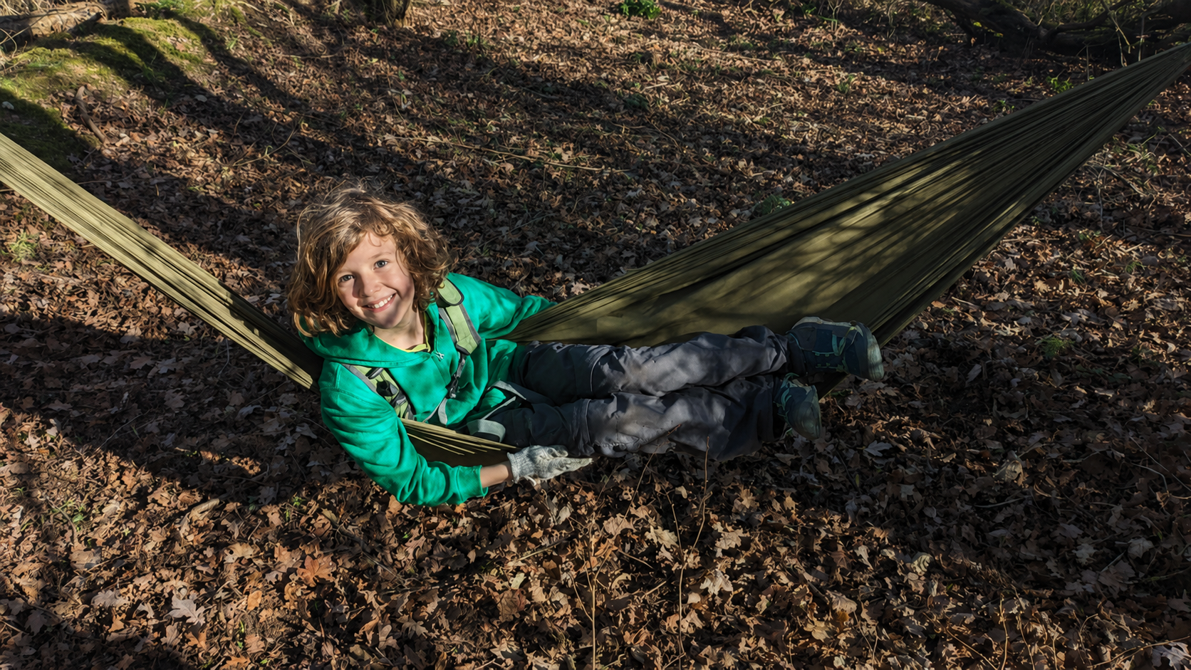 A child relaxing in a hammock among the autumn leaves at our woodland site