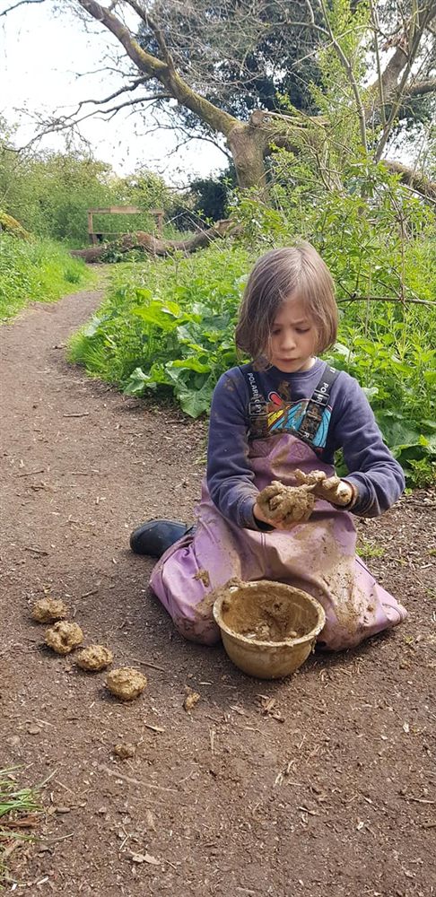 A child rolling mud balls on the woodland path